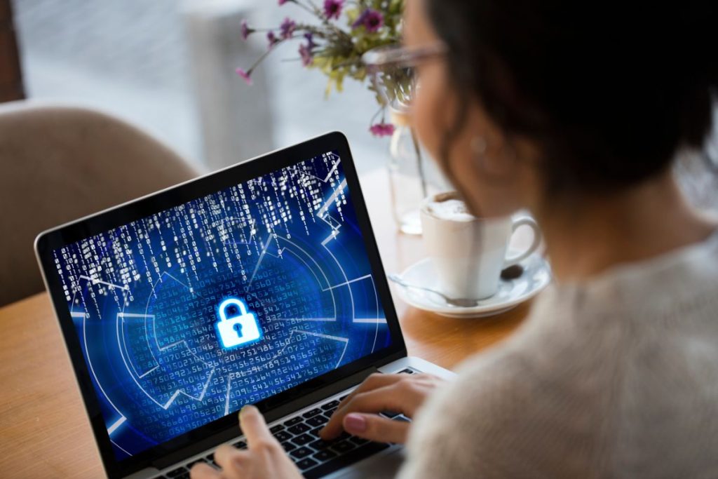 Person using laptop with digital cybersecurity lock interface on screen in home office setting