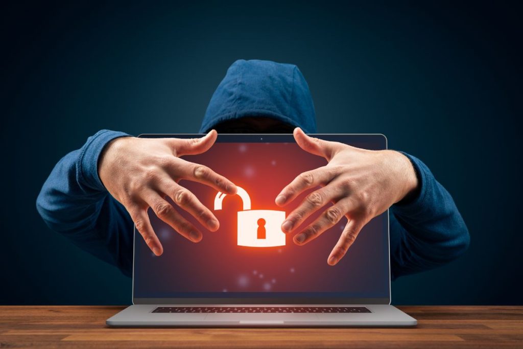 Hooded cyber attacker holding laptop with unlocked security icon